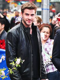 a man in black leather jacket standing next to a bunch of people on the street