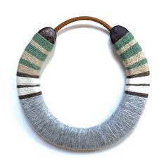 a gray and green striped knitted necklace with wooden bead on white wall background