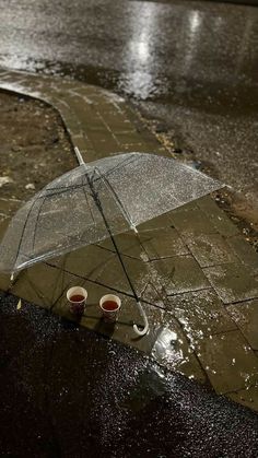 two coffee cups are placed under an umbrella in the rain