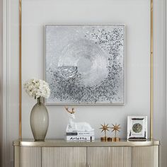 a white vase with flowers on top of a wooden cabinet in front of a painting