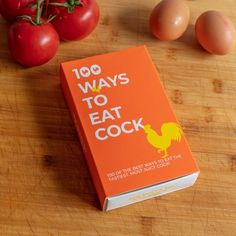 an orange book sitting on top of a wooden table next to tomatoes and egg shells