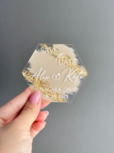 a person holding up a gold foil save the date sticker in front of a gray background