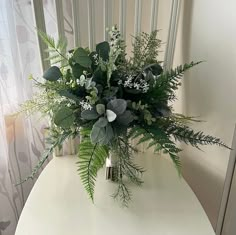 a white table topped with a vase filled with greenery