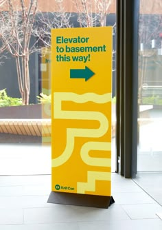 a yellow sign that says elevator to basement this way with an arrow pointing towards it