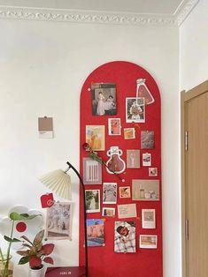 a red wall with pictures on it and a lamp next to the desk in front of it