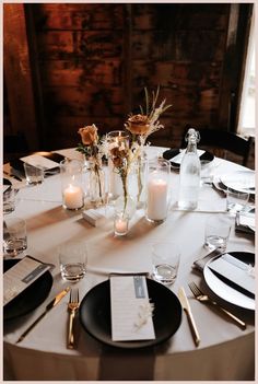 the table is set with white and black plates, silverware, candles and flowers