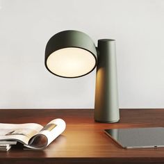 a table lamp sitting on top of a wooden desk next to a tablet computer and magazine