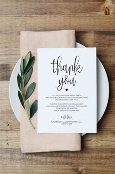 a white plate topped with a napkin next to a green leafy place card on top of a wooden table