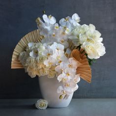 a vase filled with white and yellow flowers on top of a table next to a gray wall