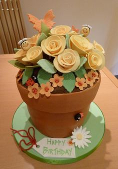 a birthday cake with flowers in a pot on top of a table next to a laptop