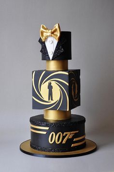 a black and gold cake with a golden bow tie on it's top tier