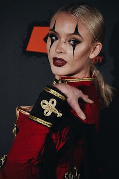 a woman with makeup on her face wearing a red dress and gold trimmings