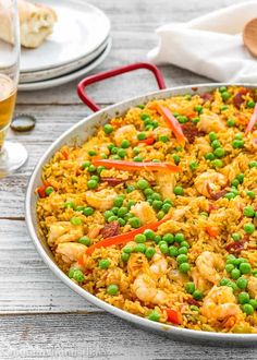 a large pan filled with rice and shrimp next to two glasses of beer on a table