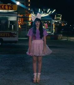 a woman standing in the middle of an amusement park at night wearing a bunny ears hat