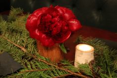 a red flower sitting on top of a table next to a candle and some branches