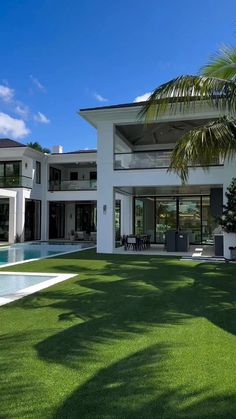 a large white house with a pool in the front yard and palm trees around it