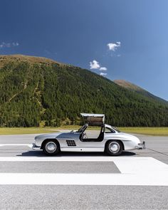 a car parked in front of a mountain with its door open and the roof down