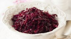 a white bowl filled with red cabbage on top of a table next to a spoon