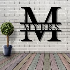 a metal letter m on a brick wall next to a potted plant and wooden floor