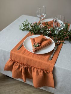 a place setting with orange linens and greenery