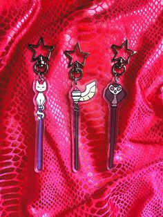 three keychains with cartoon characters on them sitting on a red cloth covered surface