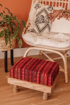 a white chair with a red and black cushion on top of it next to a potted plant