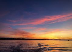 the sun is setting over the water with clouds in the sky