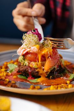 a person is holding a fork over a plate of food with vegetables and meat on it