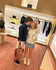 a man and woman are kissing in front of a display case with clothes on mannequins