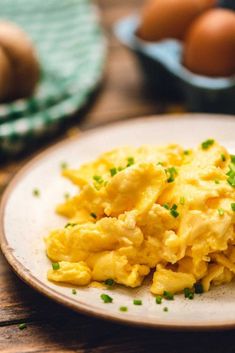 scrambled eggs on a white plate with chives and an egg in the back ground