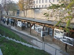 people are looking at pictures on display in an enclosed area with trees and buildings behind them