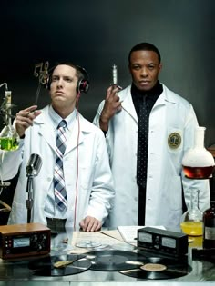 two men in white lab coats are standing next to each other with headphones on