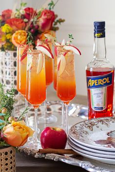 two glasses filled with drinks sitting on top of a table next to plates and flowers