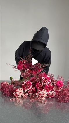 a person in a black hoodie is surrounded by pink flowers and greenery on a table