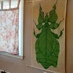 a green bug is hanging on the wall next to a window with red and white curtains