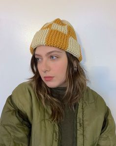 a young woman wearing a knitted hat and green jacket is looking at the camera