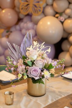 a vase filled with purple flowers on top of a table next to balloons and candles