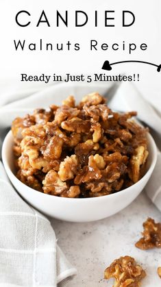 a white bowl filled with candied walnuts on top of a table next to a napkin