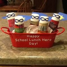 a red bucket filled with school lunch items on top of a counter next to a sign that says happy school lunch hero day