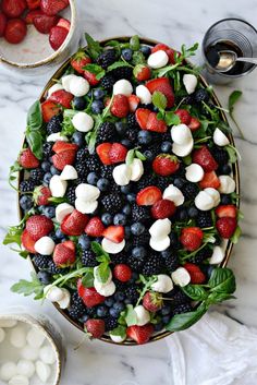 a platter filled with berries, mozzarella and spinach on top of a marble table