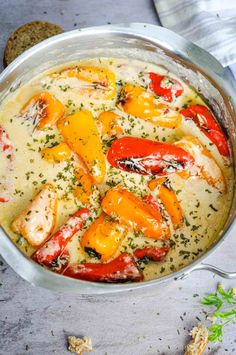 a pan filled with chicken and peppers on top of a table next to some bread