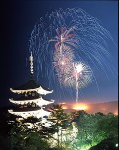 fireworks are lit up in the night sky above a building with a pagoda on top