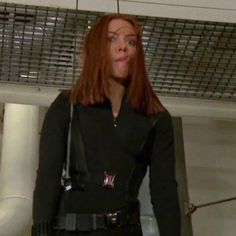 a woman with red hair wearing a black suit and holding her hands on her hips