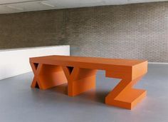 an orange bench sitting on top of a cement floor next to a white brick wall