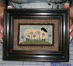 a woman holding up a framed painting with sheep on it