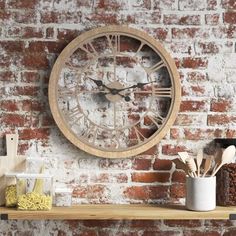 a clock mounted to the side of a brick wall above a shelf with utensils