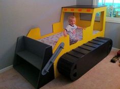 a toddler is sitting on a bed made to look like a construction truck,