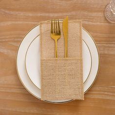 a white plate topped with a gold fork and knife next to a burlap napkin