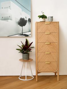 a wooden dresser next to a painting and potted plant