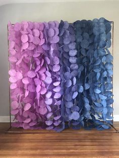 purple and blue paper flowers are displayed in a glass case on a wooden floor next to a wall